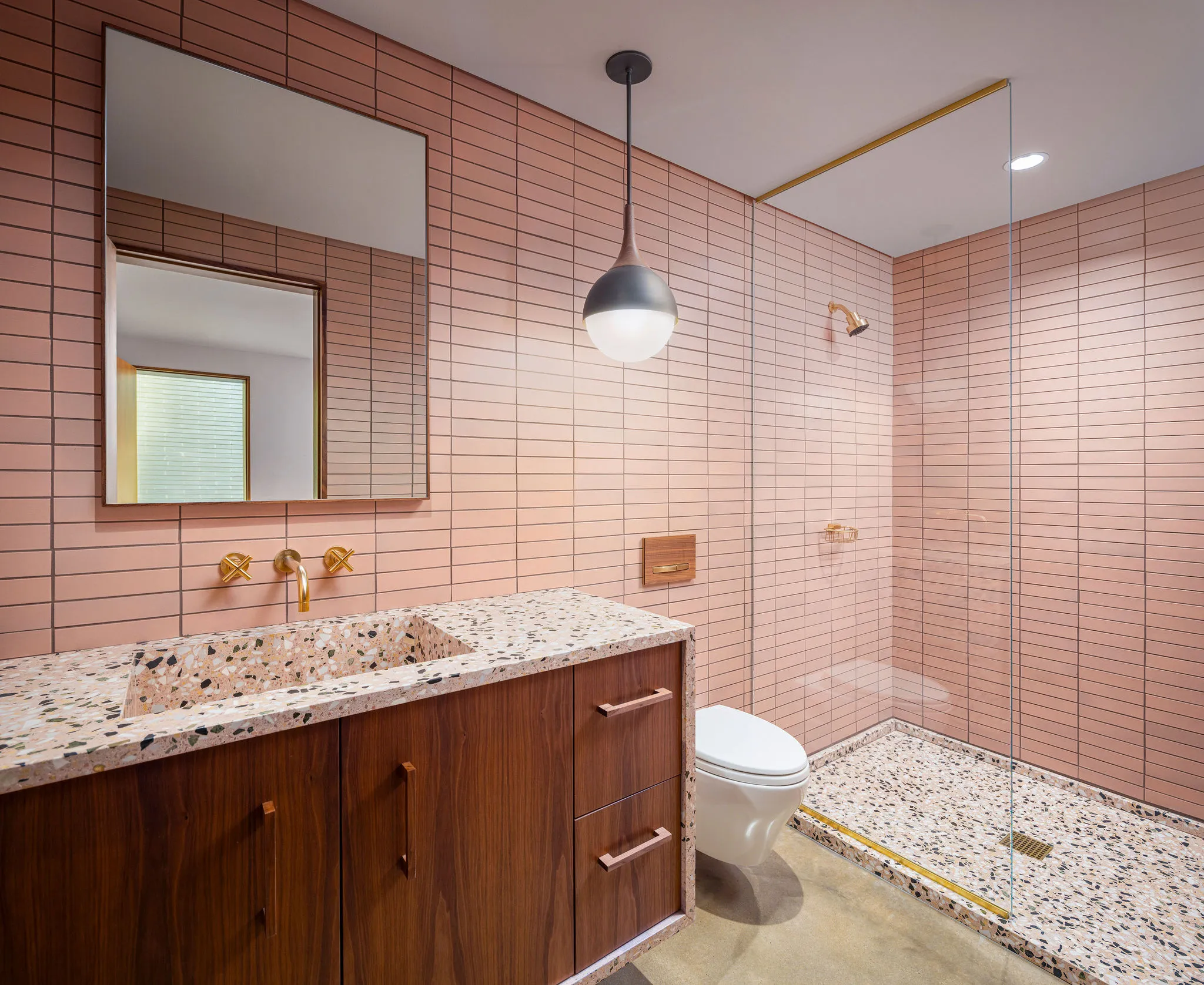 Bath with blush stacked tile, a terrazzo integrated sink on a walnut vanity, brass fixtures, and a curbless shower