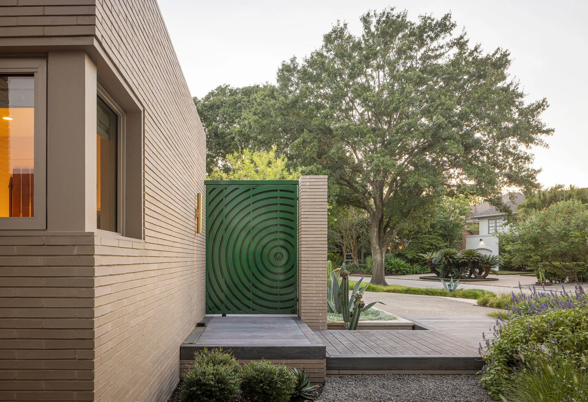 Green laser-cut steel gate with a concentric ripple pattern opening from the brick wall onto an ipe deck