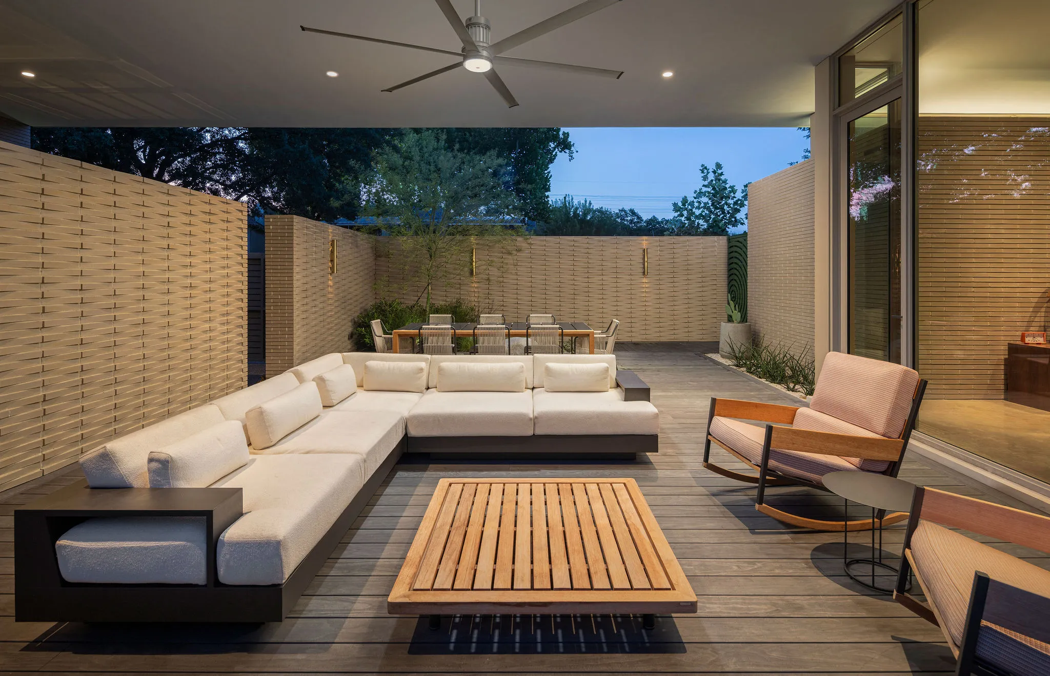 Covered terrace with a white sectional, teak coffee table, and rockers, enclosed by woven-brick screen walls