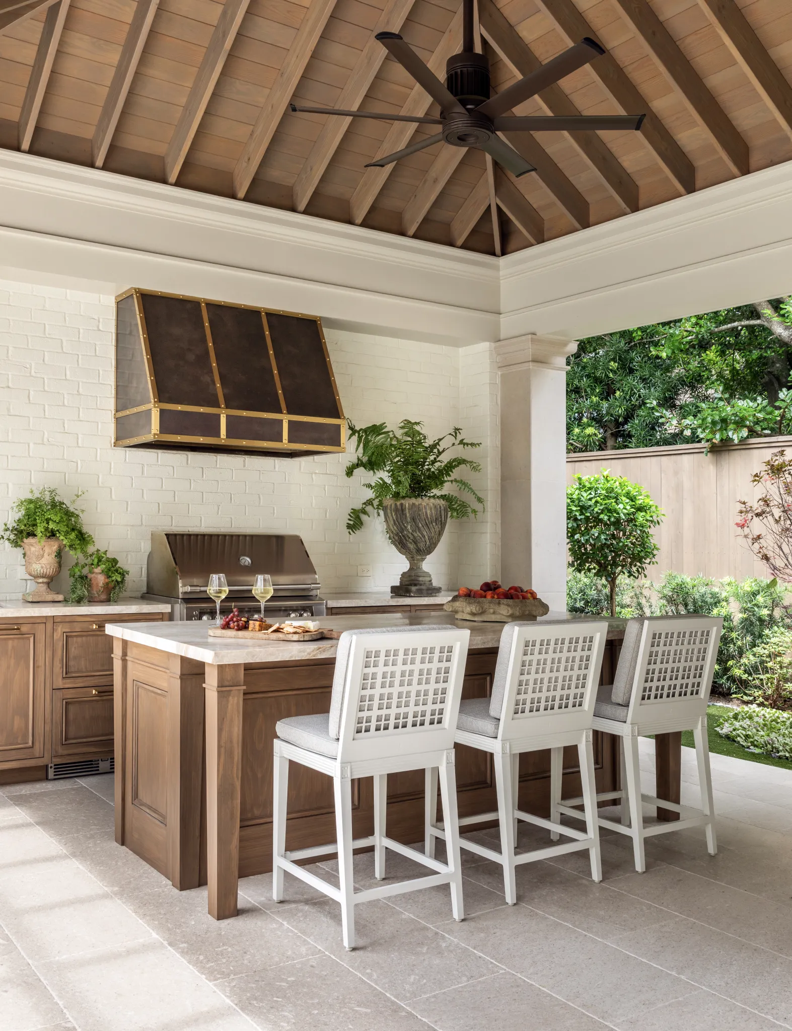 Outdoor kitchen with a walnut island, white lattice barstools, and a bronze range hood