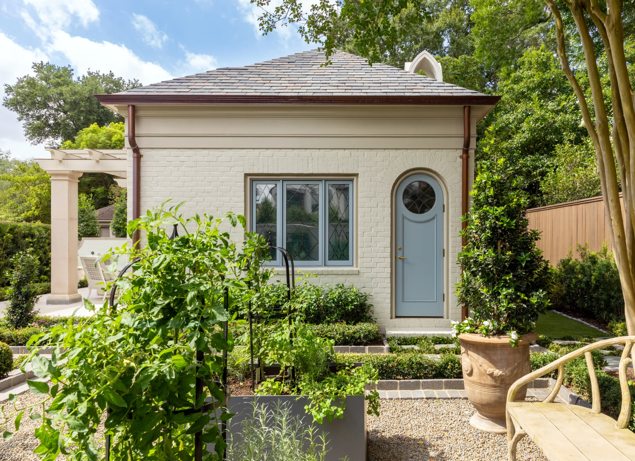 Pool house facade with leaded-glass windows, arched door, and terracotta urn