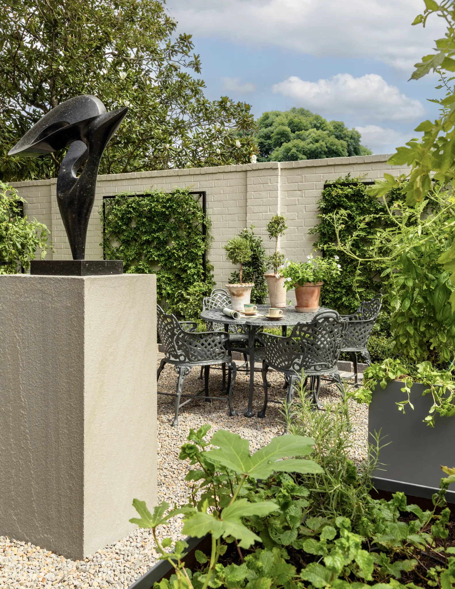 Gravel courtyard with a bronze sculpture, iron bistro table, and espaliered walls